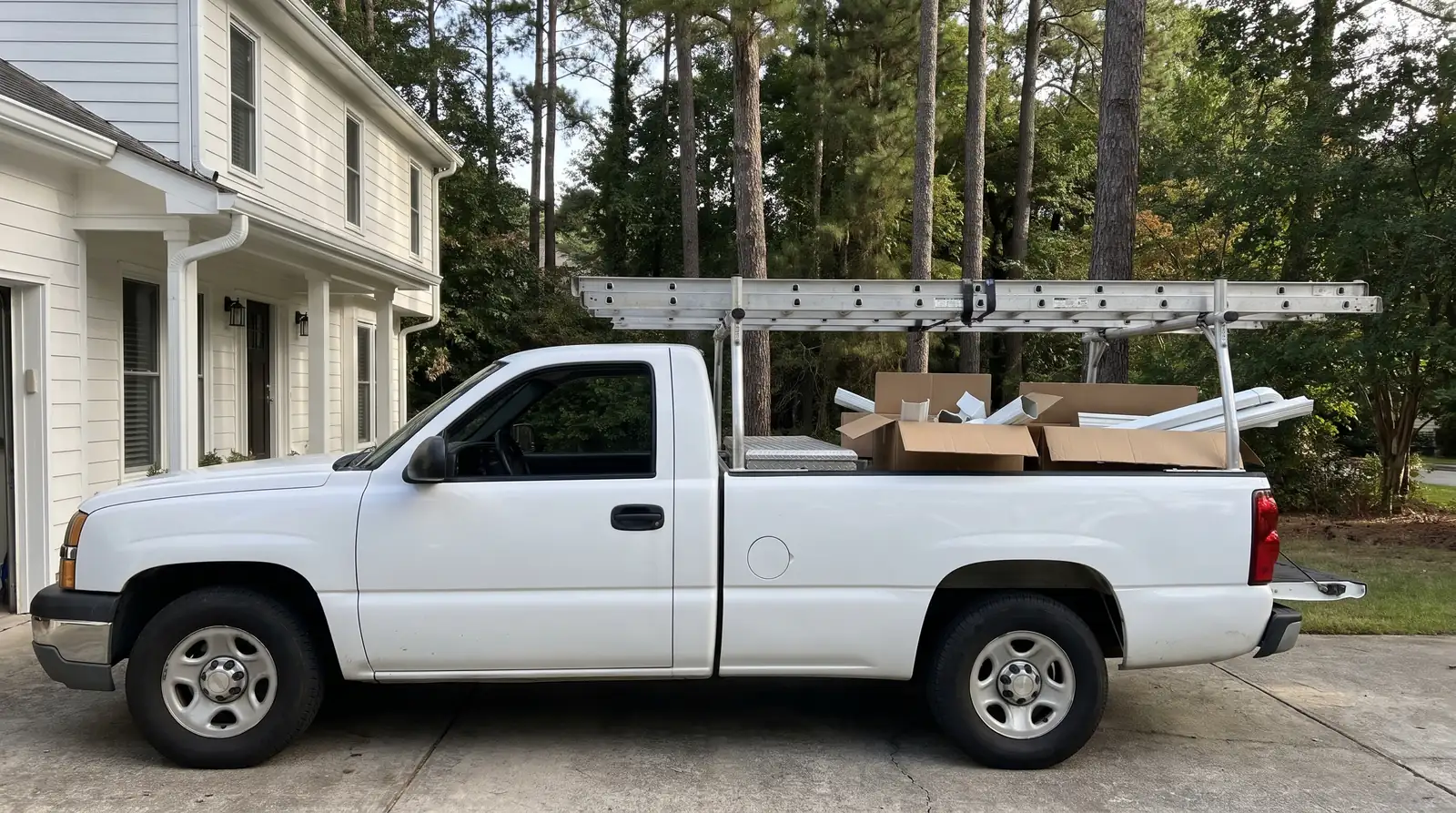 White work pickup with ladders on a rack and boxes of gutter parts in the bed