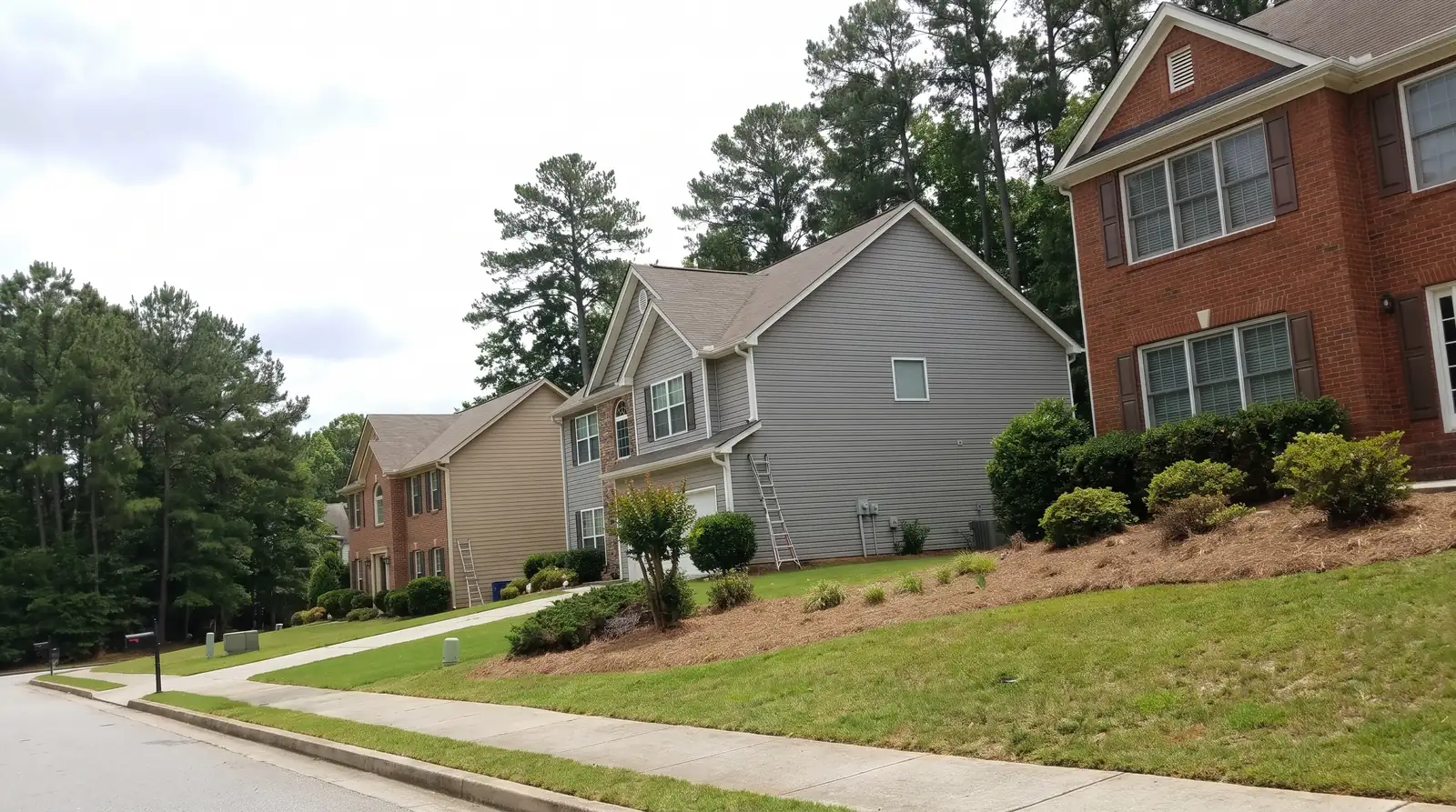 Brick and vinyl-sided two-story houses with gutters along a wooded suburban street