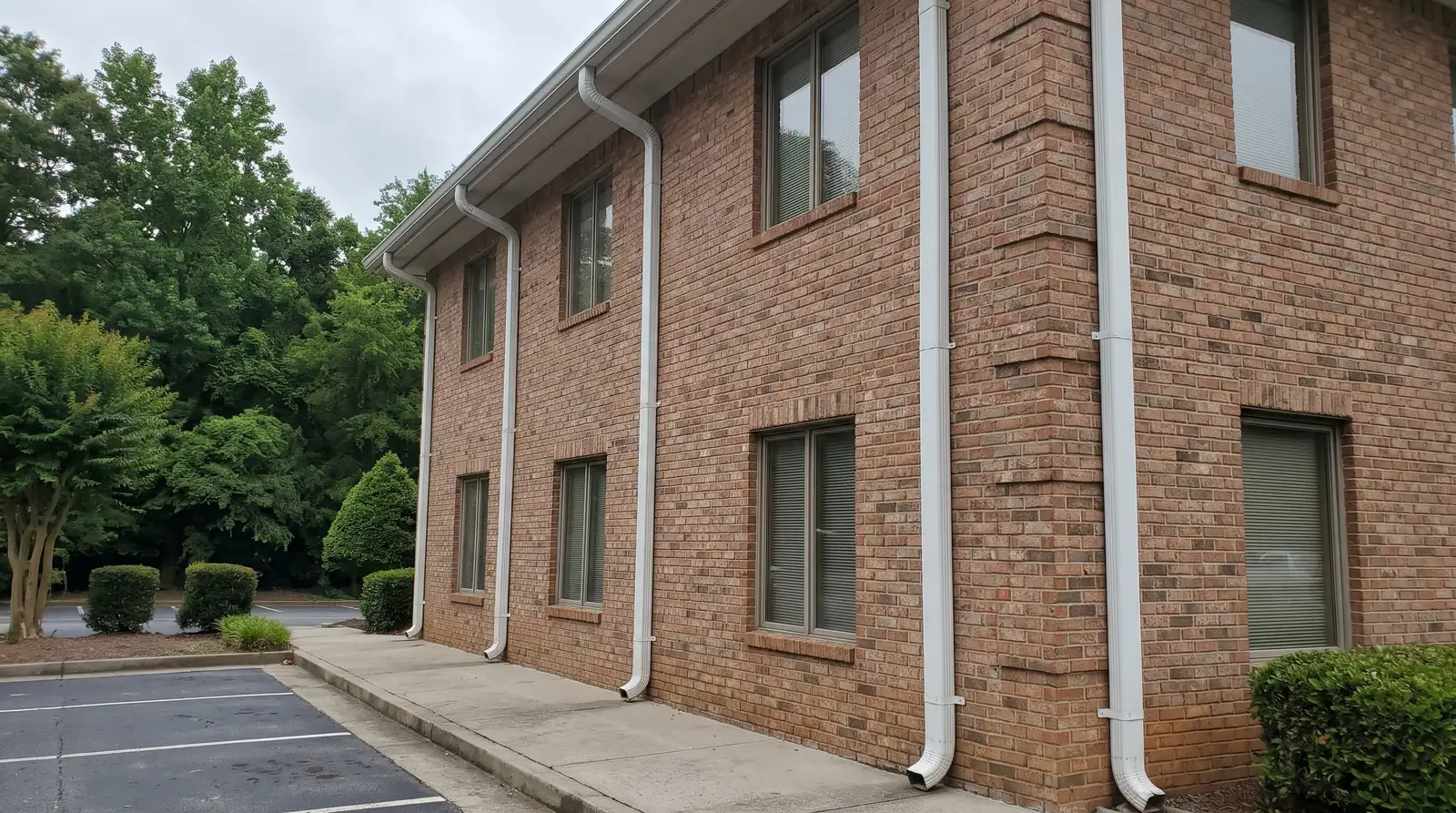 Two-story brick office building with white gutters and downspouts beside a parking lot
