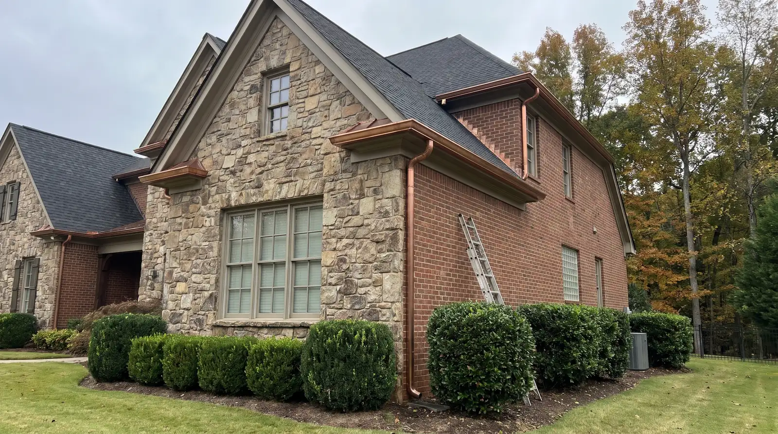 Stone and brick house with copper gutters and downspouts behind trimmed boxwoods