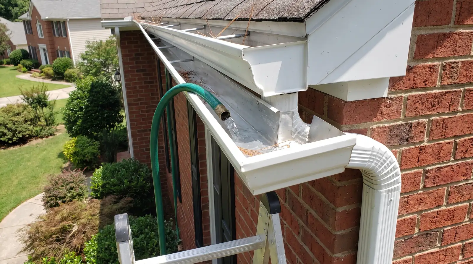 Garden hose flushing water along a clean white gutter toward the downspout